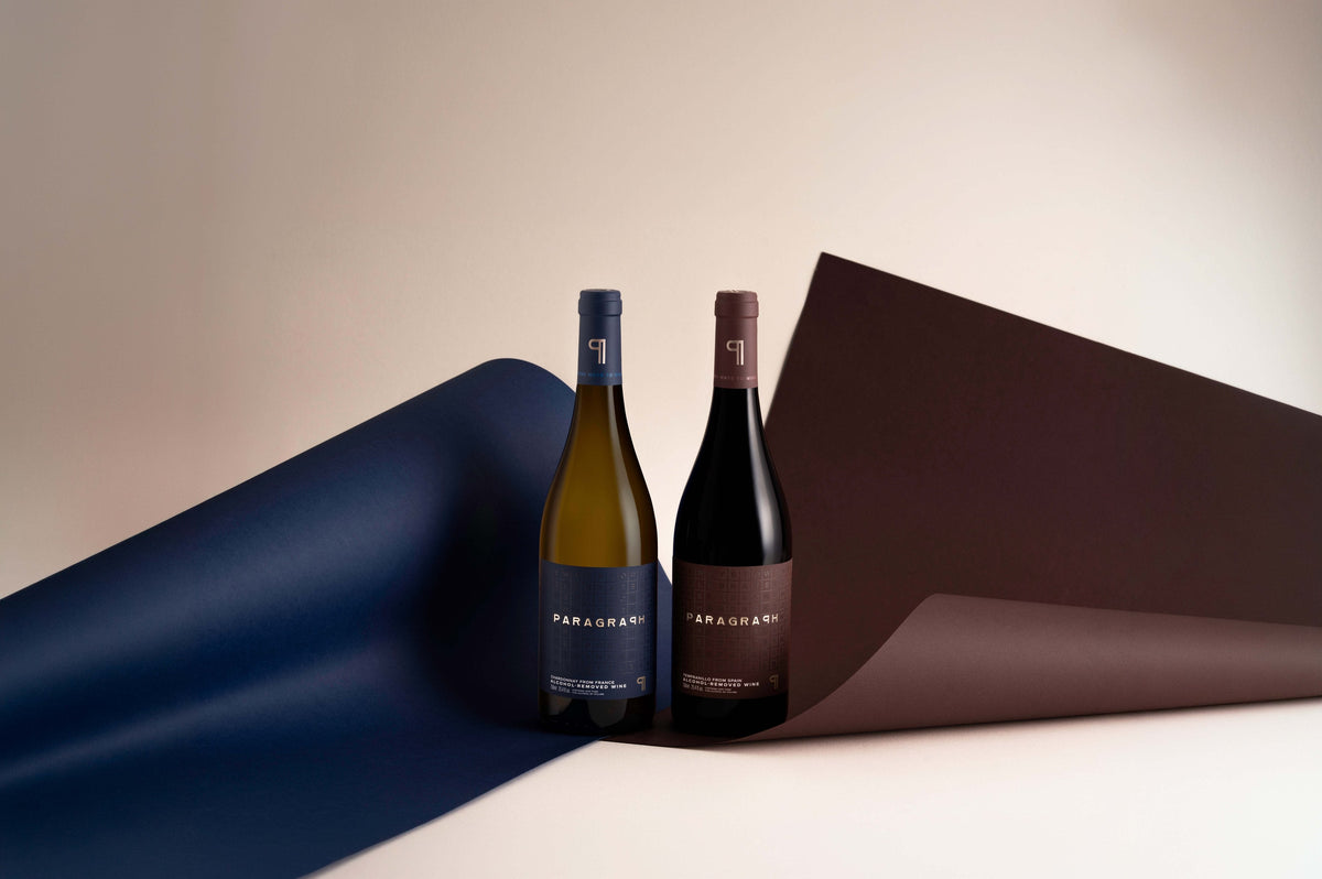A bottle of PARAGRAPH Chardonnay and a bottle of PARAGRAPH Tempranillo standing between navy and oxblood paper